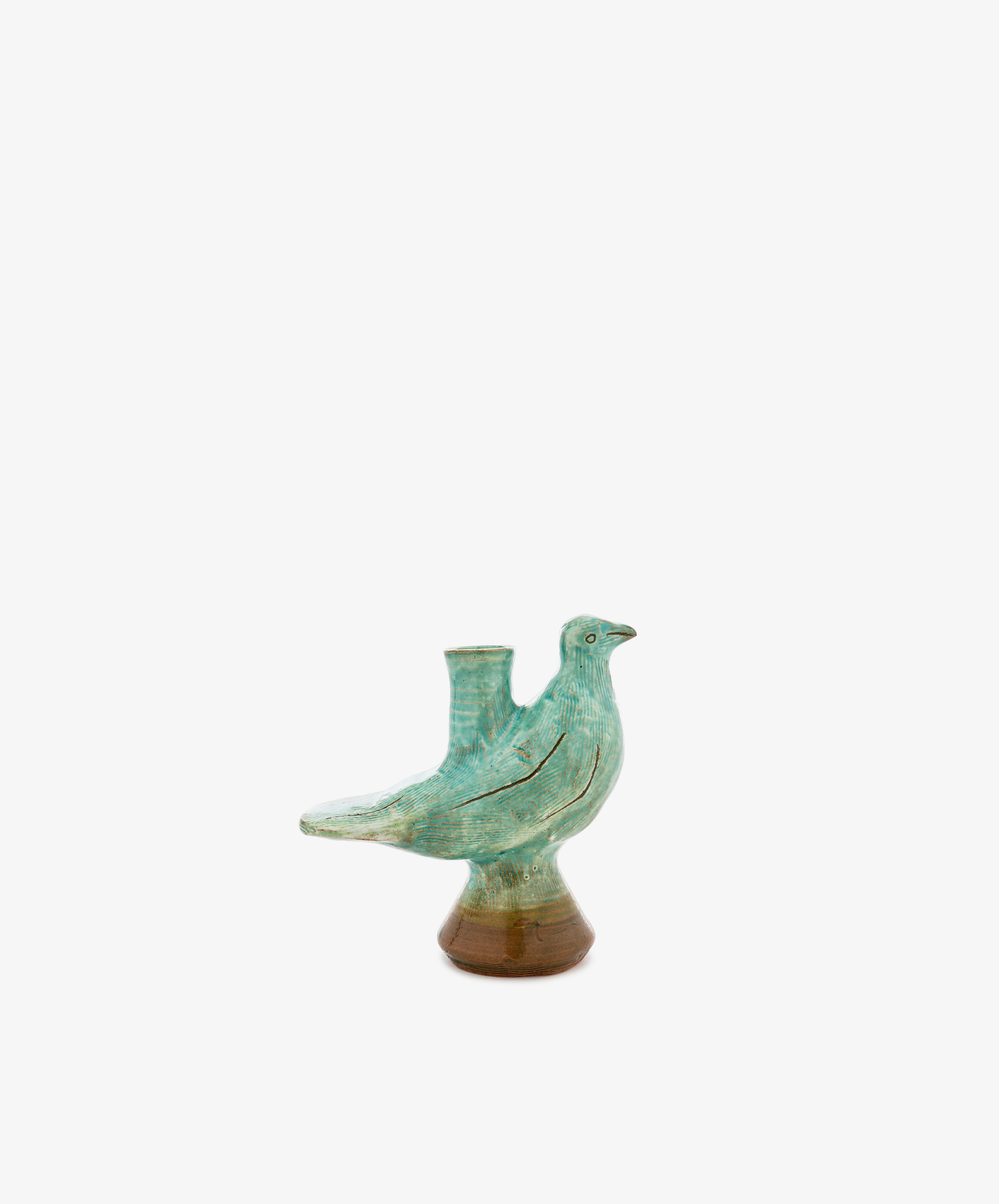 The Peace Dove Candle Holder, crafted from ceramic with a sage green glaze and a brown base, features an opening on its back and is displayed atop a decorative pedestal against a plain white background.