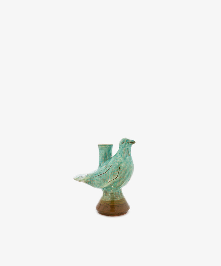 The Peace Dove Candle Holder features a ceramic vessel shaped like a bird, finished in a sage green glaze that highlights its elegant form. A small cylindrical opening on its back makes it perfect for holding a candle, creating an ideal accent piece for a decorative pedestal or shelf. Set against a plain white background, this unique holder is both functional and stylish.