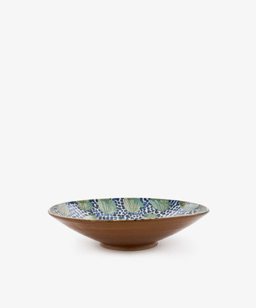 The Green Leaves Serving Bowl is a wide, shallow handmade bowl featuring a brown exterior and an interior adorned with green leaves and a blue dot pattern on a white background, inspired by traditional Fayoum pottery.