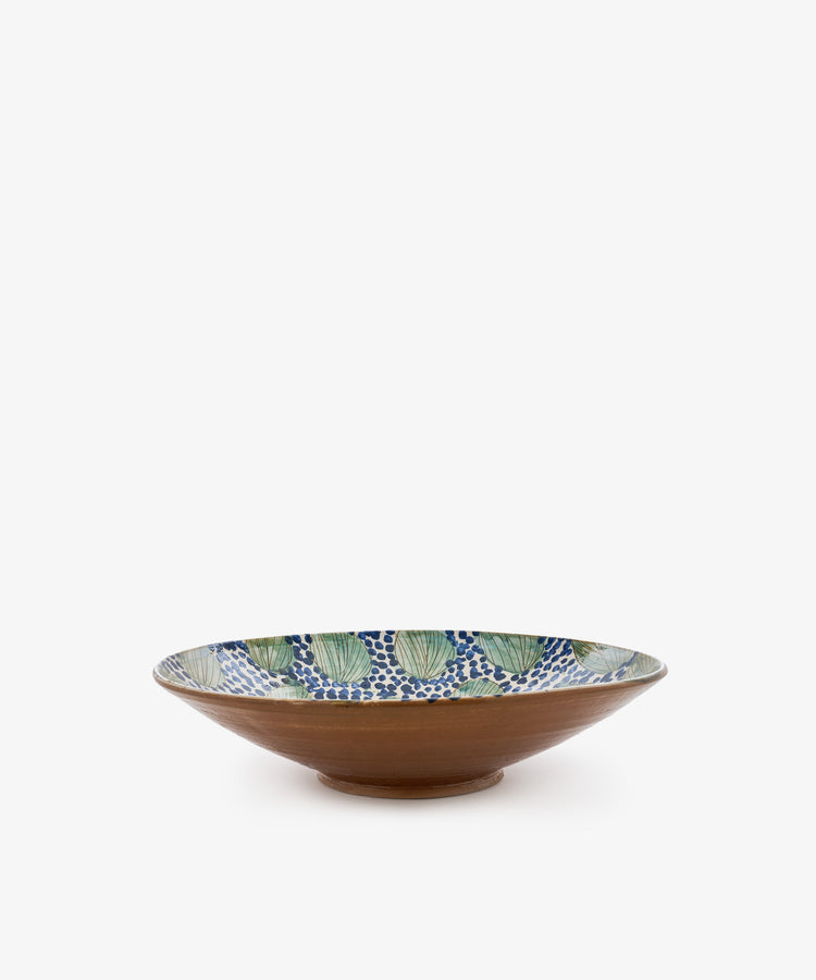 The Green Leaves Serving Bowl is a wide, shallow handmade bowl featuring a brown exterior and an interior adorned with green leaves and a blue dot pattern on a white background, inspired by traditional Fayoum pottery.