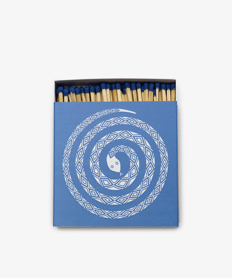 A blue box of Luxury Matches features a white spiral Magic Snake design and is partially open to reveal wooden matches with blue tips inside.