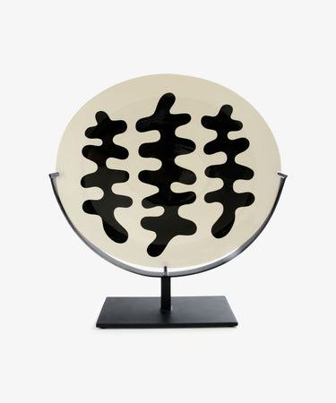 The Motif 2, Oval is a decorative white oval plate with abstract black wavy shapes, showcased upright on a metal stand with a black rectangular base—a striking modernist piece for fans of unique decorative platters.