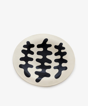An oval, off-white ceramic plate called Motif 2, featuring three abstract black wavy shapes in the center that evoke a modern geometric style.