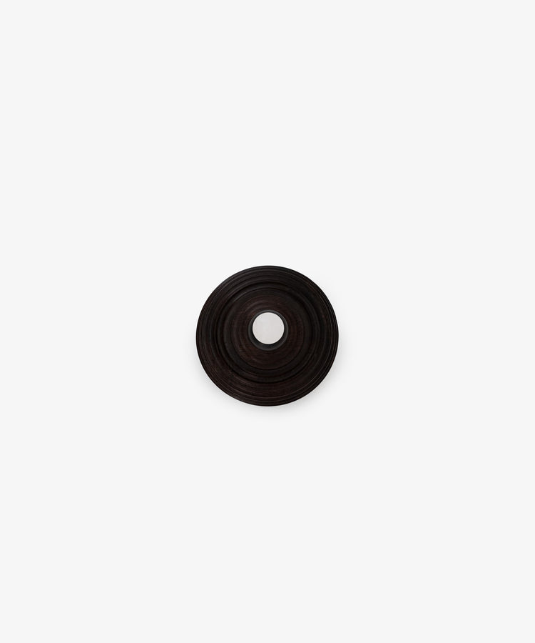 The Curiosity Box is a dark, circular African wood box with concentric ridges and a central hole, shown from above on a plain white background.