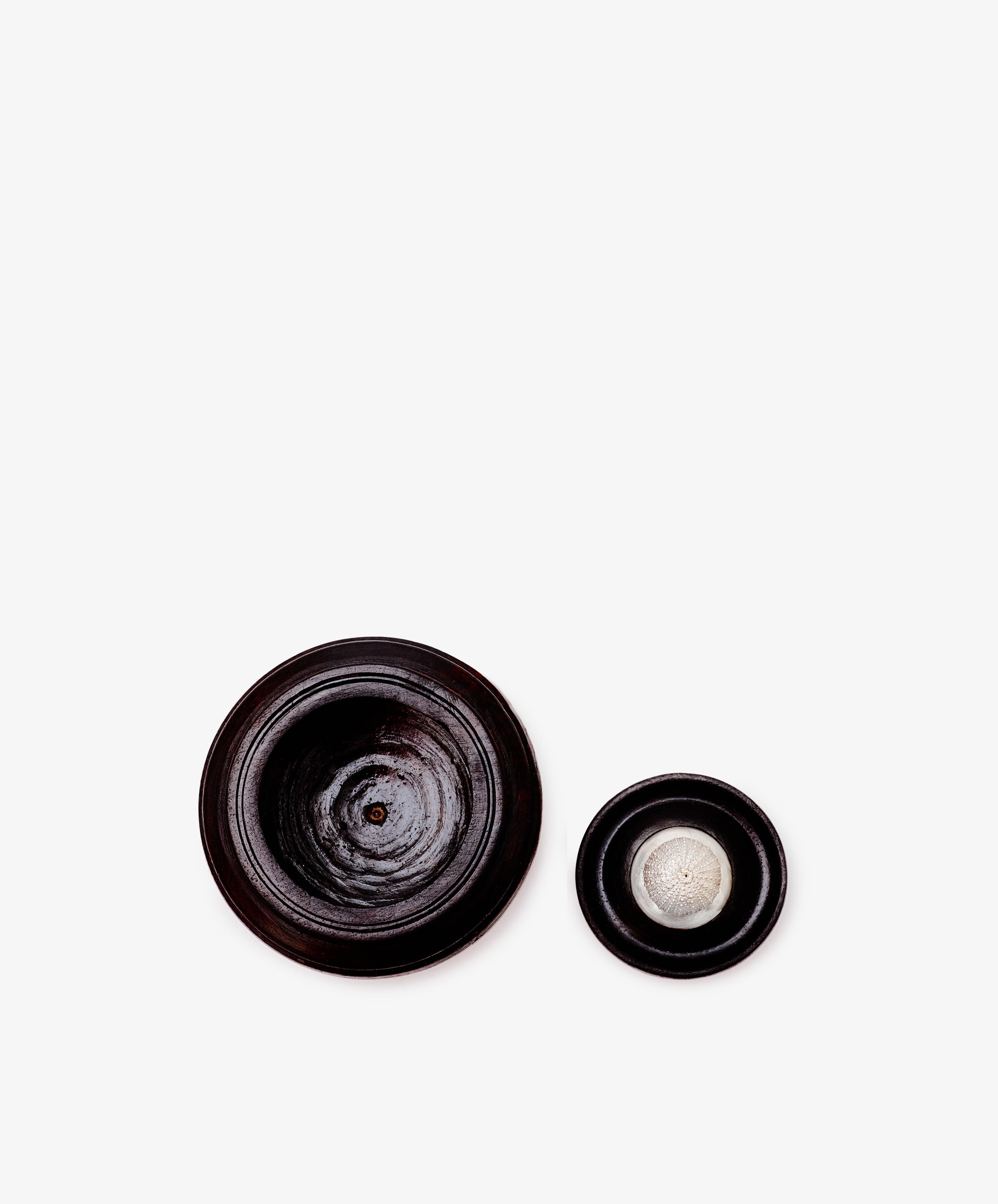 Two round, dark African wood Curiosity Boxes on a white background; the larger box is empty and the smaller holds a single clove of garlic—perfect as a unique collectible keepsake box.