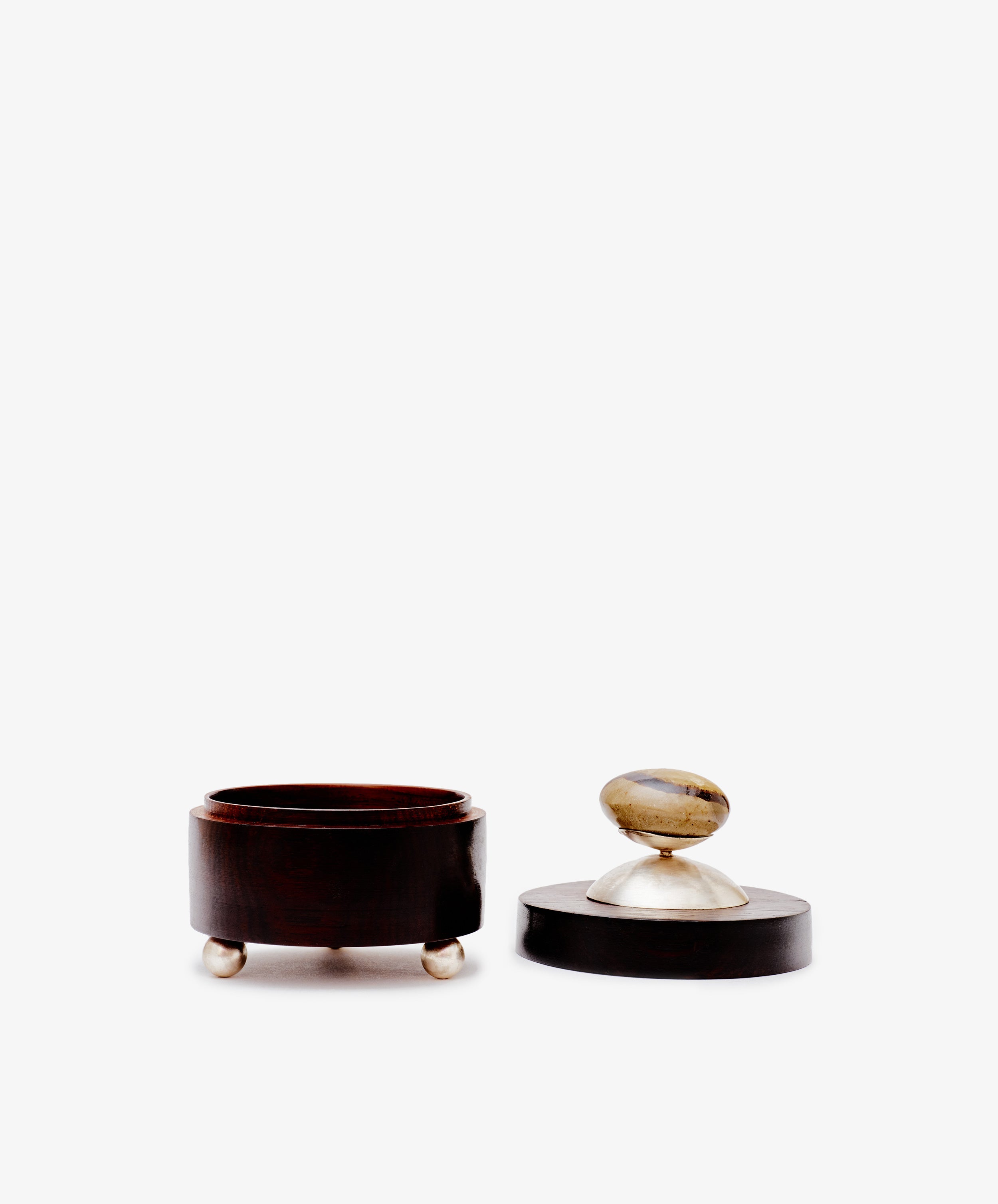 The Curiosity Box is a round African wood box with three small metal feet and a matching lid topped with a stone handle, shown against a white background.