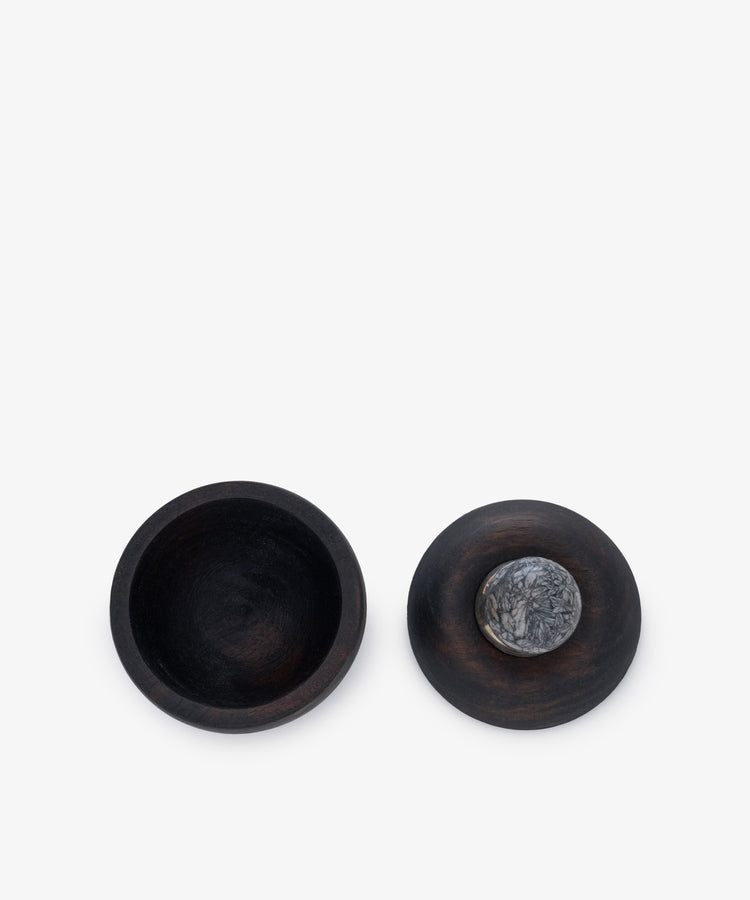 Curiosity Box 15: Two round, dark African wood boxes—one open to reveal its empty interior, the other closed with a lid topped by a small, round gray stone handle—reflect timeless vintage craftsmanship.