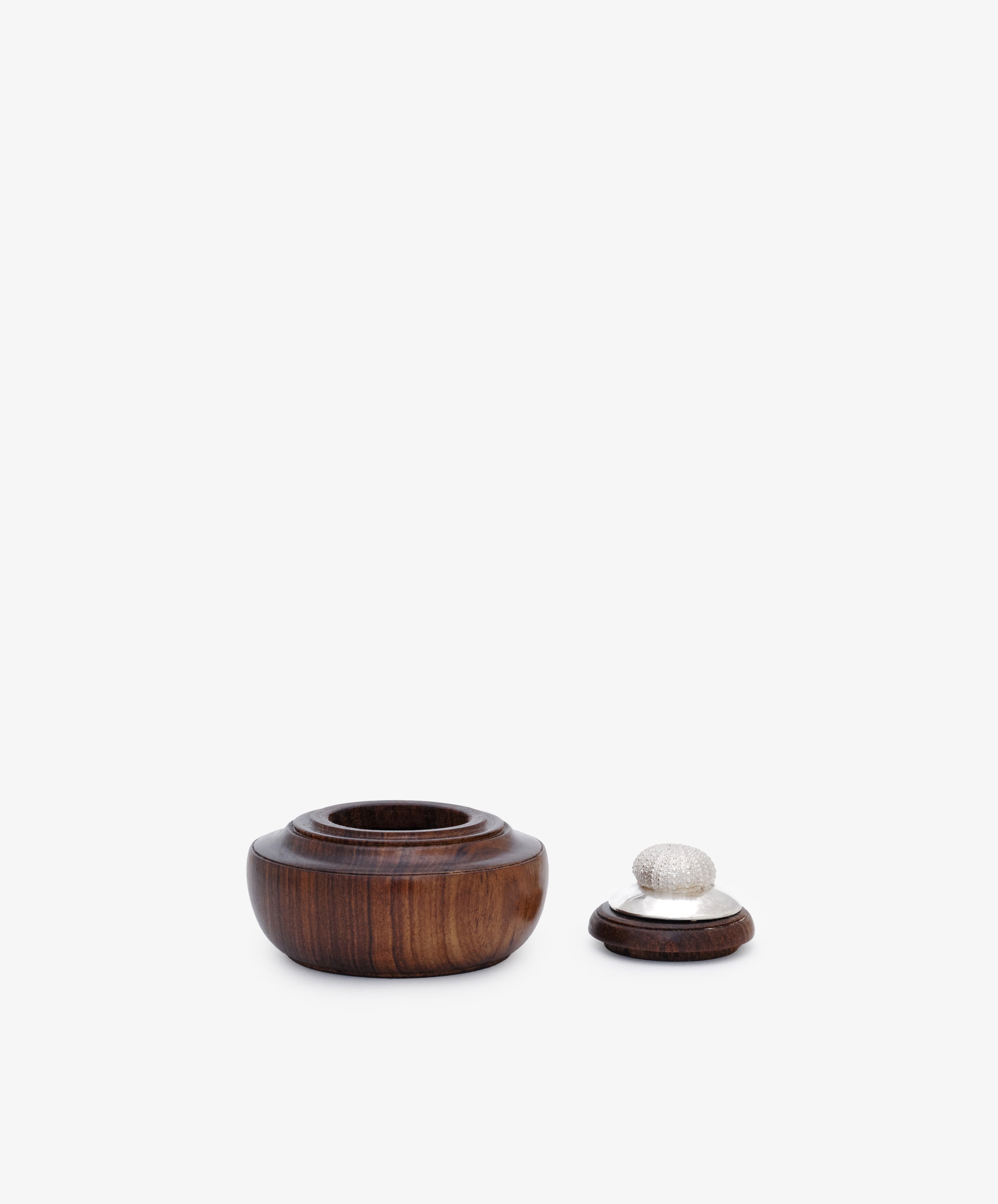 The Curiosity Box 16, a small round African wood box with a separate lid and silver decorative knob, is displayed on a plain white background.