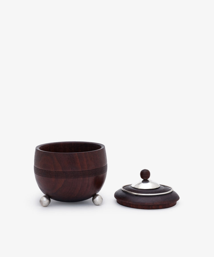 Curiosity Box 17: A small, round African wood box with metal feet and a matching lid featuring a metal knob, shown with the lid beside the container—an elegant piece from the Antje Weber collection.
