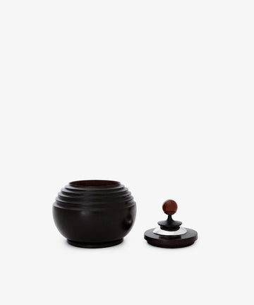 The Curiosity Box, a round dark African wood container with a grooved design, is displayed with its matching lid beside it on a plain white background.