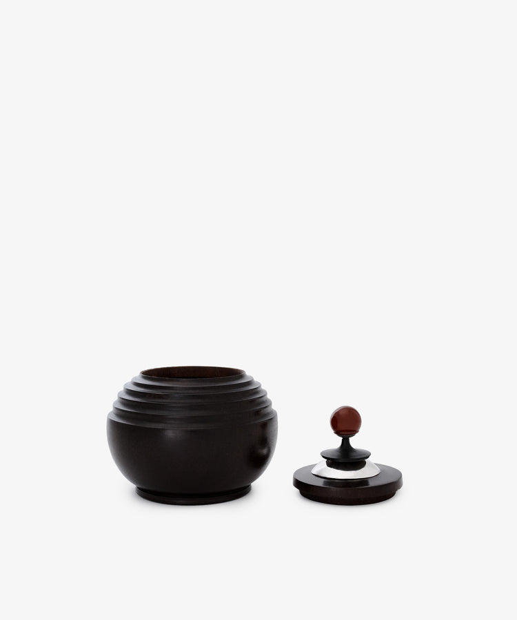 The Curiosity Box, a round dark African wood container with a grooved design, is displayed with its matching lid beside it on a plain white background.