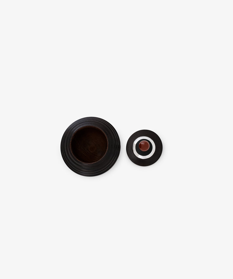 Two black Curiosity Boxes, circular in shape, are displayed on a white surface: the larger box sits empty on the left, while the smaller one on the right holds a red item.