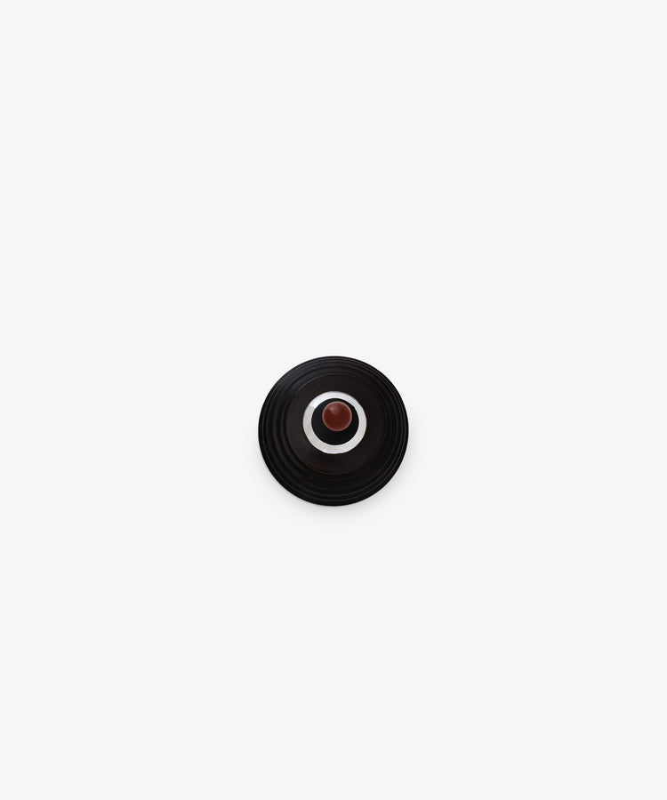 The Curiosity Box, a small round black object with concentric rings and a central brown dot, is centered on a plain white background.
