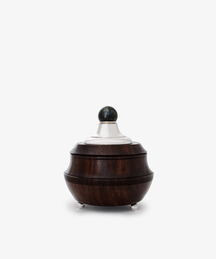 The Curiosity Box is a restored vintage round container crafted from dark African wood with sterling silver accents—a silver lid, spherical knob, and three elegant feet—shown against a plain white background.
