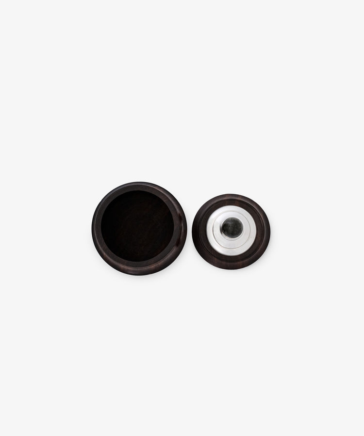 The Curiosity Box is a round, dark African wood box shown open with its lid beside it, revealing sterling silver accents on the metal insert beneath the lid.