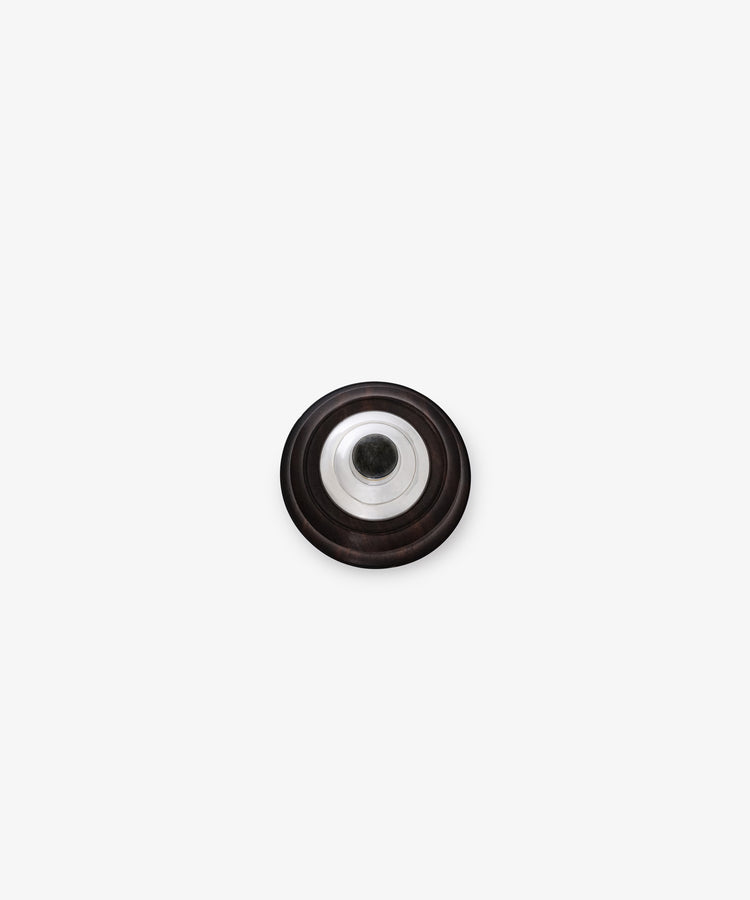 The Curiosity Box is a round, black metallic disc with sterling silver accents and a central hole, shown from above on a plain white background.