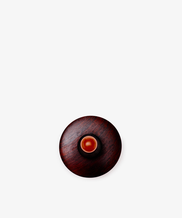 The Curiosity Box, a dark African wood box, is topped with a small round amber object and displayed against a plain white background.