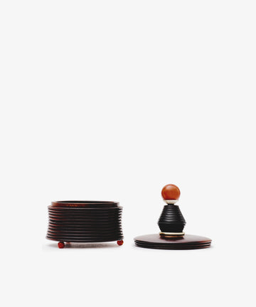 The Curiosity Box, crafted from dark African wood with red feet, is displayed open with its matching lid—featuring a round wooden knob—set beside it on a white background.