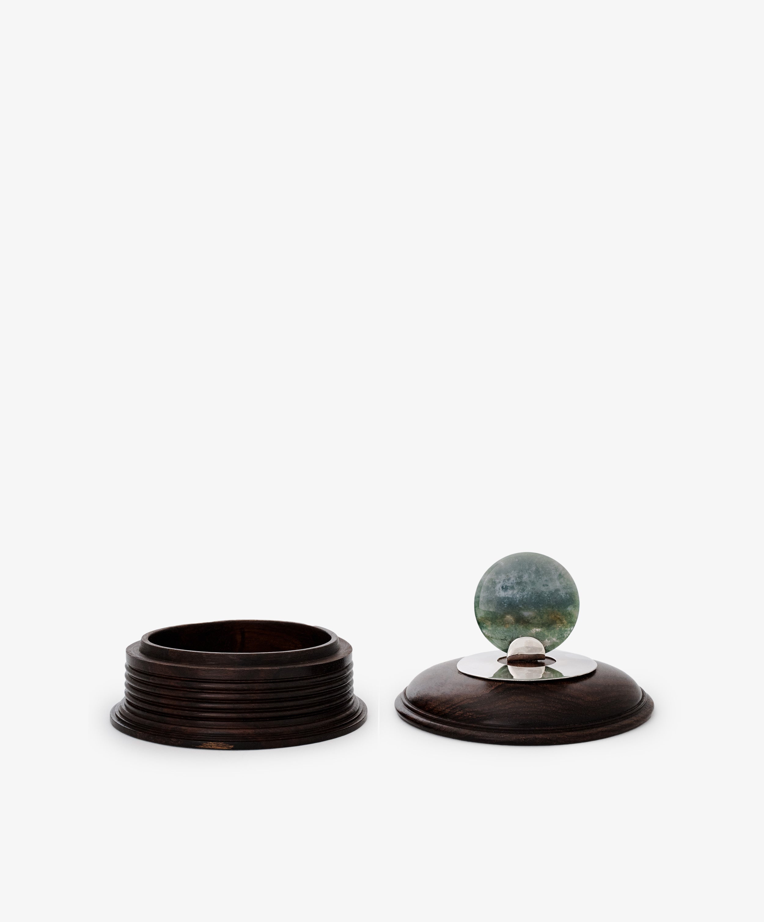 The Curiosity Box is a restored round vintage African wood container. Its removable lid features a metal accent topped with a greenish-blue marble, making it an eye-catching keepsake.