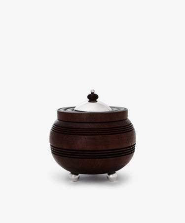 The Curiosity Box is a round African wood box with horizontal grooves, featuring a silver metal lid, knob, and three small silver feet—an artisan keepsake that stands out beautifully against a white background.