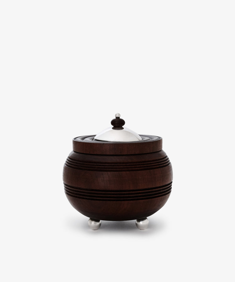 The Curiosity Box is a round African wood box with horizontal grooves, featuring a silver metal lid, knob, and three small silver feet—an artisan keepsake that stands out beautifully against a white background.