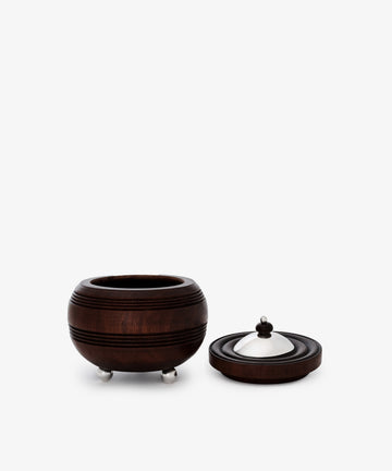 The Curiosity Box, a round African wood keepsake with three metal feet and a matching lid featuring a metal dome and wooden knob, is displayed on a plain white background—an artisan-crafted treasure.
