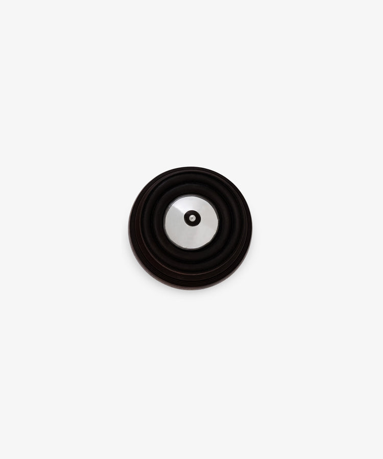 The Curiosity Box, a round metallic object with a black circular rim, sits centered on a white background—its design reminiscent of an artisan keepsake box and evoking a sense of timeless appeal.