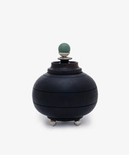 Curiosity Box 2: A round black African wood box with a lid, silver feet, and a green spherical handle on top, displayed against a plain white background.