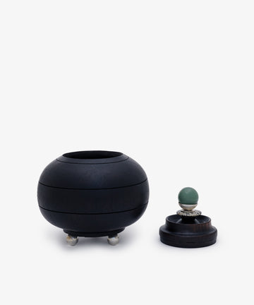 The Curiosity Box 2, a round black keepsake box with three small feet, is shown next to its matching lid topped with a green spherical handle—adding unique charm to this restored vintage piece.