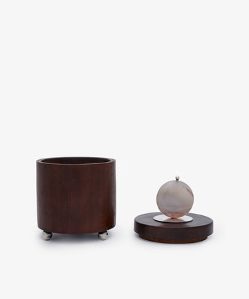 Curiosity Box 3: A cylindrical African wood box with a separate lid, round stone handle, and small metal feet—displayed on a white background. Ideal as a unique keepsake or art piece.