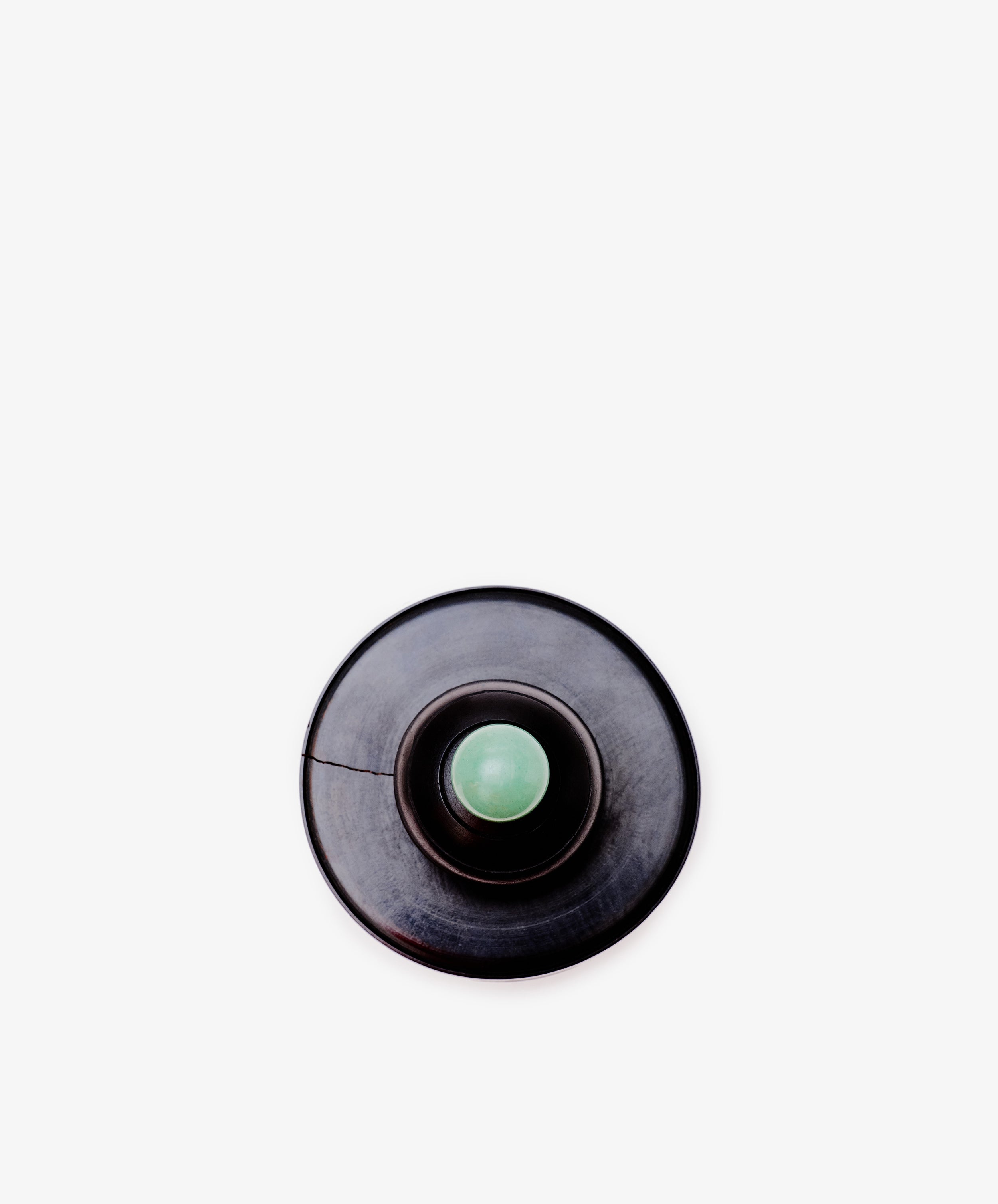 The Curiosity Box features a round, dark-colored button with a light green center, inspired by Antje Weber's art style, set against a plain white background.