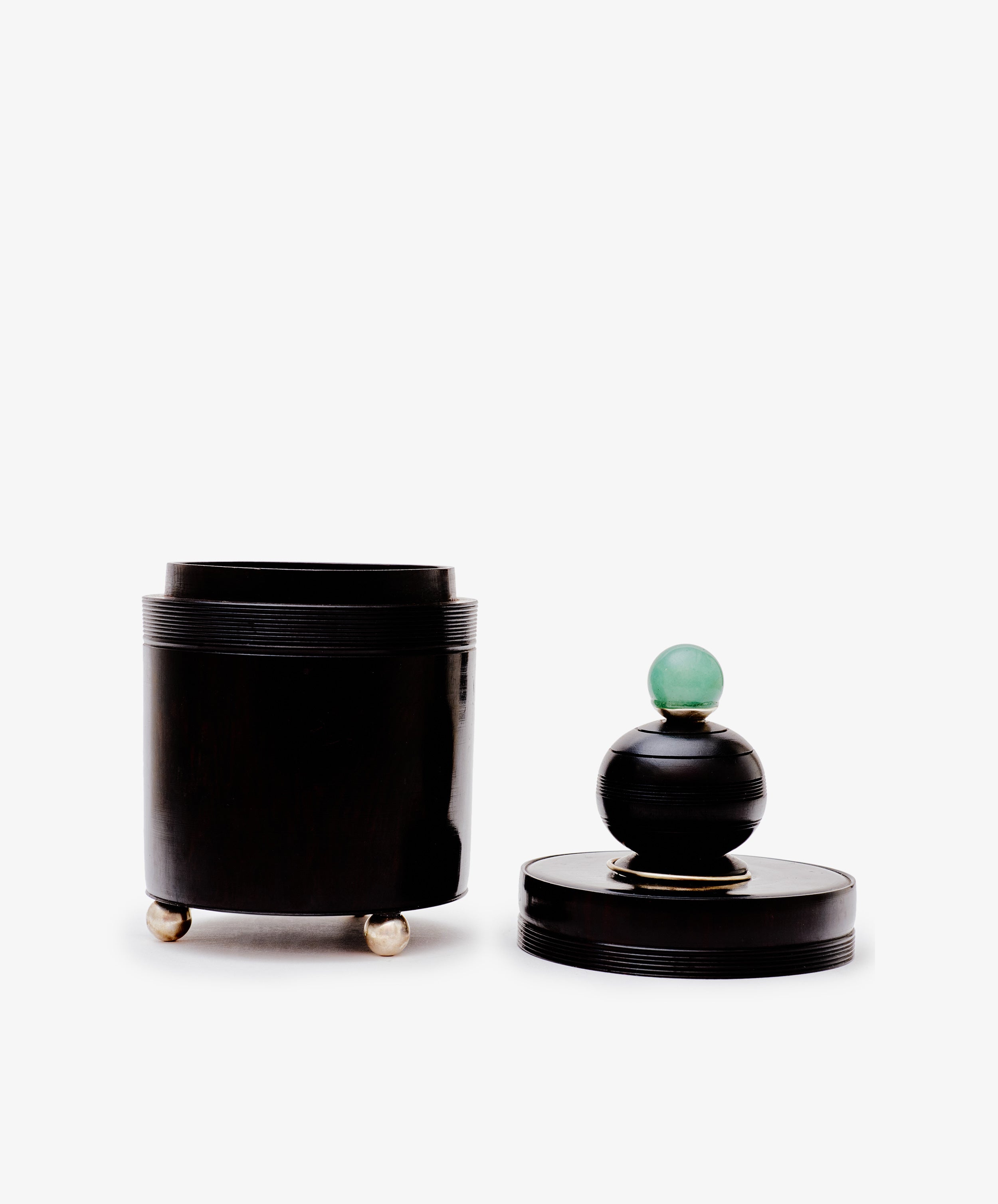 The Curiosity Box is a black cylindrical African wood box with three small metallic feet and a detached lid, featuring a round black handle topped with a green sphere, shown against a white background.