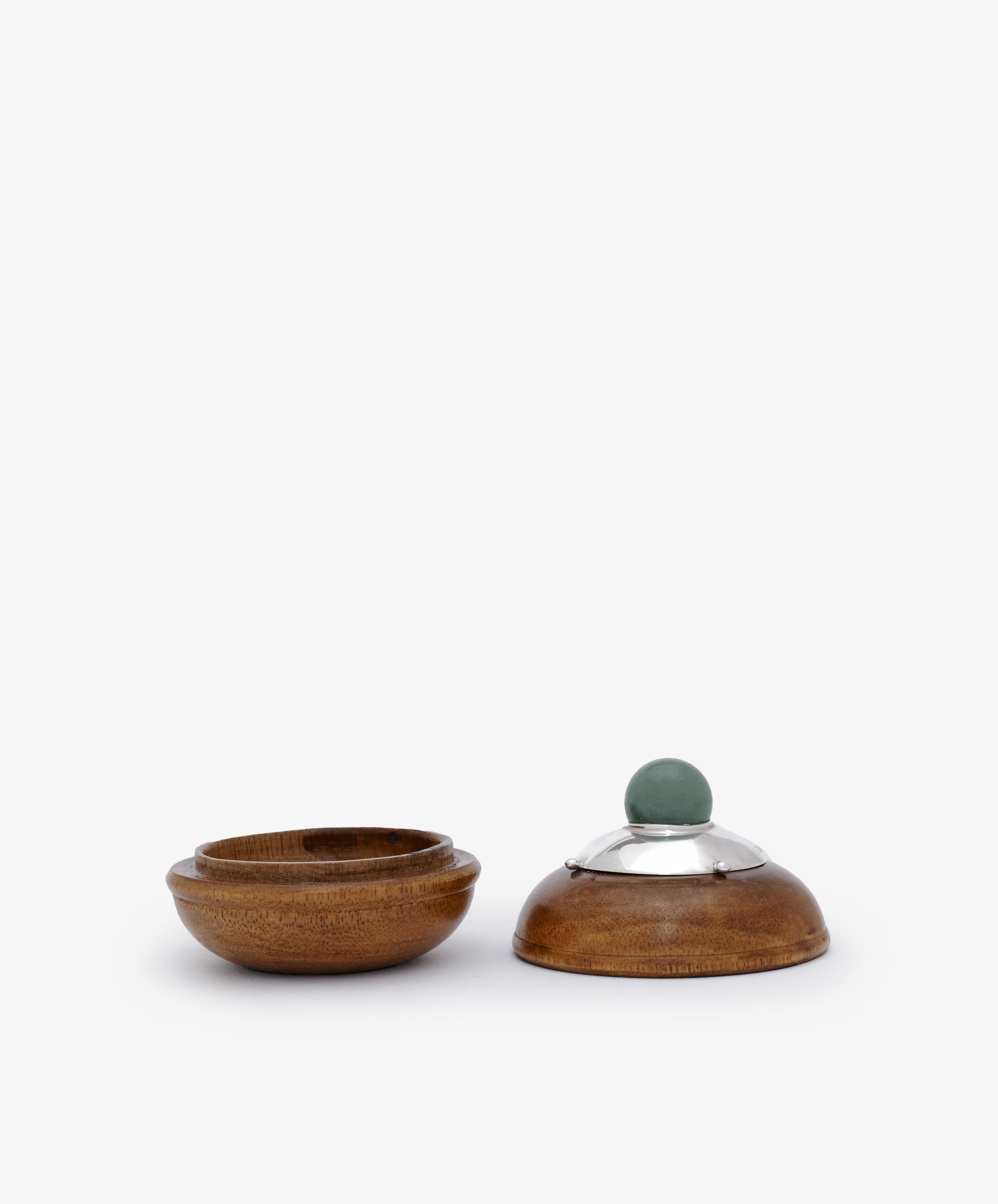 Curiosity Box 6: a small round African wood box with an open base on the left and a lid with a silver rim and green knob on the right, displayed on a plain white background.