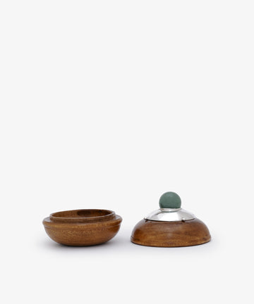 Curiosity Box 6: a small round African wood box with an open base on the left and a lid with a silver rim and green knob on the right, displayed on a plain white background.