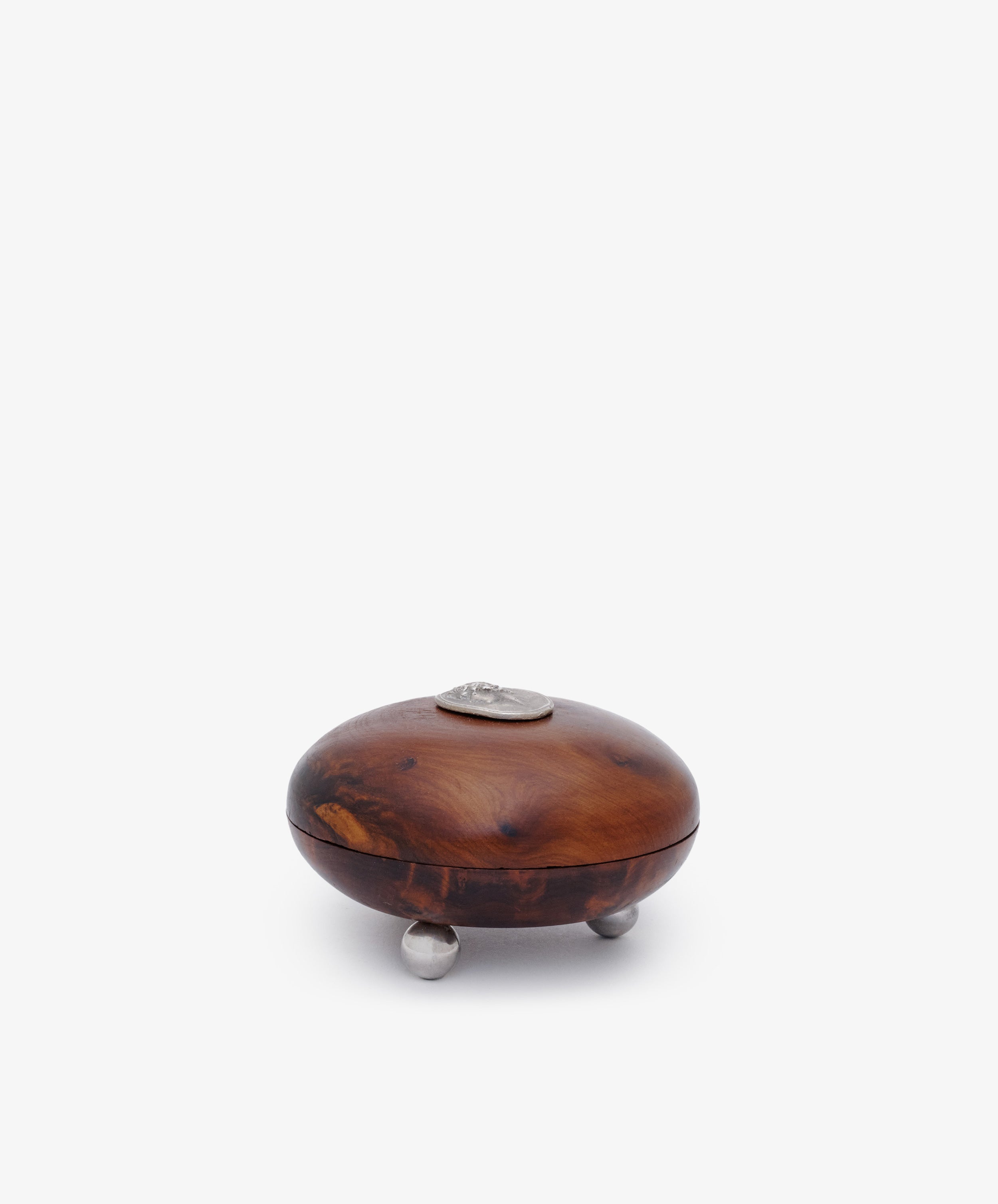 Curiosity Box 7 is a round African wood box with a lid, featuring a silver accent on top and three small metal feet, shown against a plain white background.