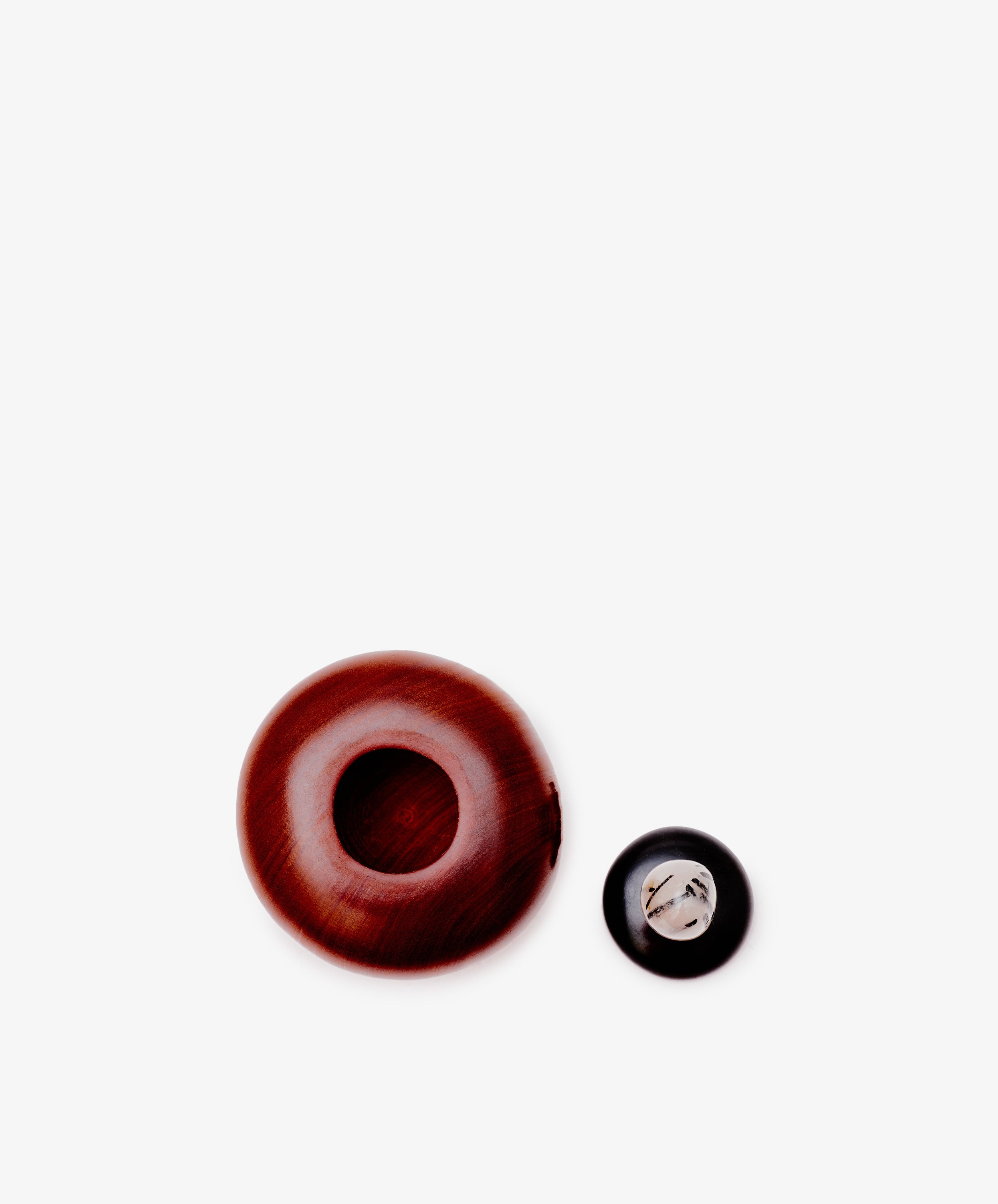 The Curiosity Box, a round brown wooden container with a hollow center, sits beside a small black and silver metallic button on a white background.