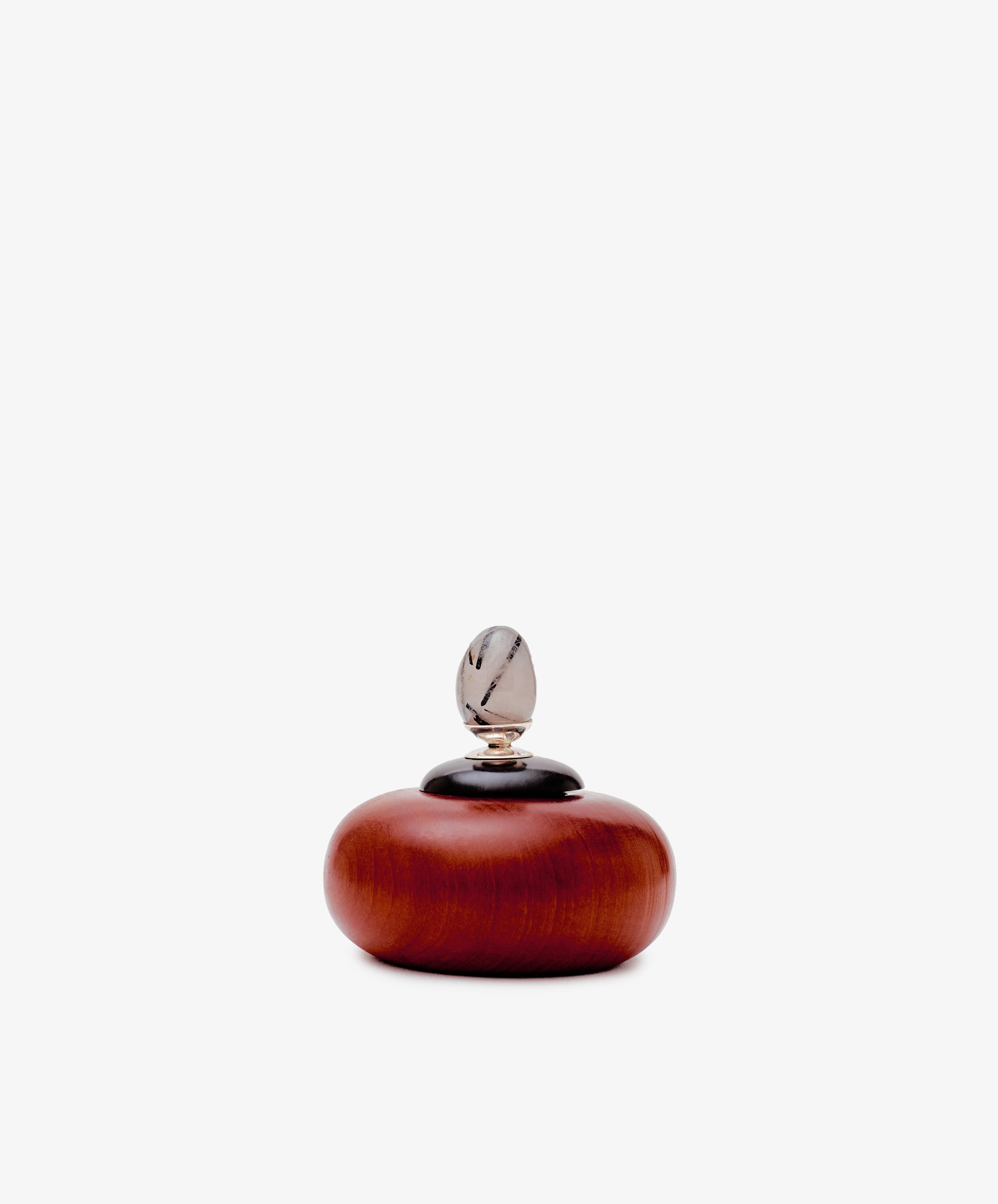 The Curiosity Box is a small, round African wood box with a smooth finish, featuring a black lid and an oval-shaped translucent ornament on top.