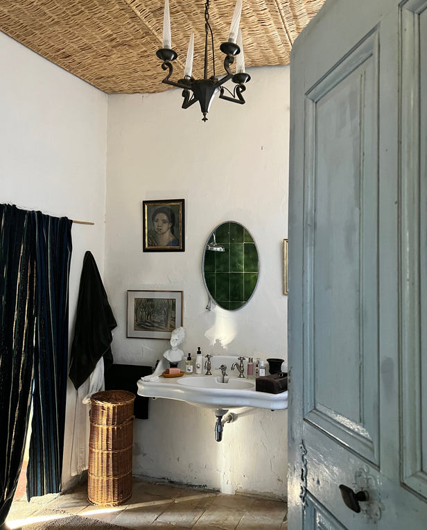 Vintage bathroom with a pedestal sink, oval mirror, wicker hamper, and framed art on the wall