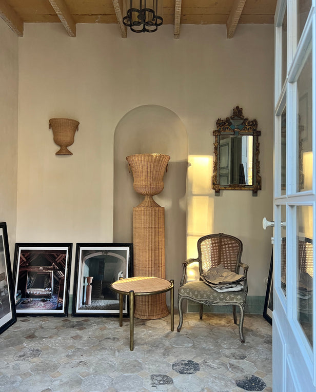 Room with wicker baskets, framed photos on the floor, a small table, and an ornate mirror on the wall