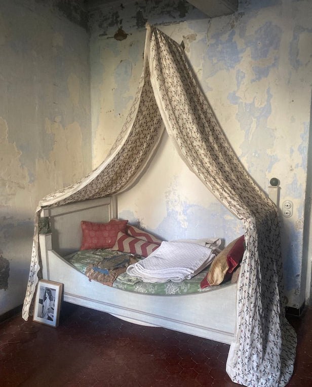 Canopy daybed with patterned pillows and blanket against a weathered wall