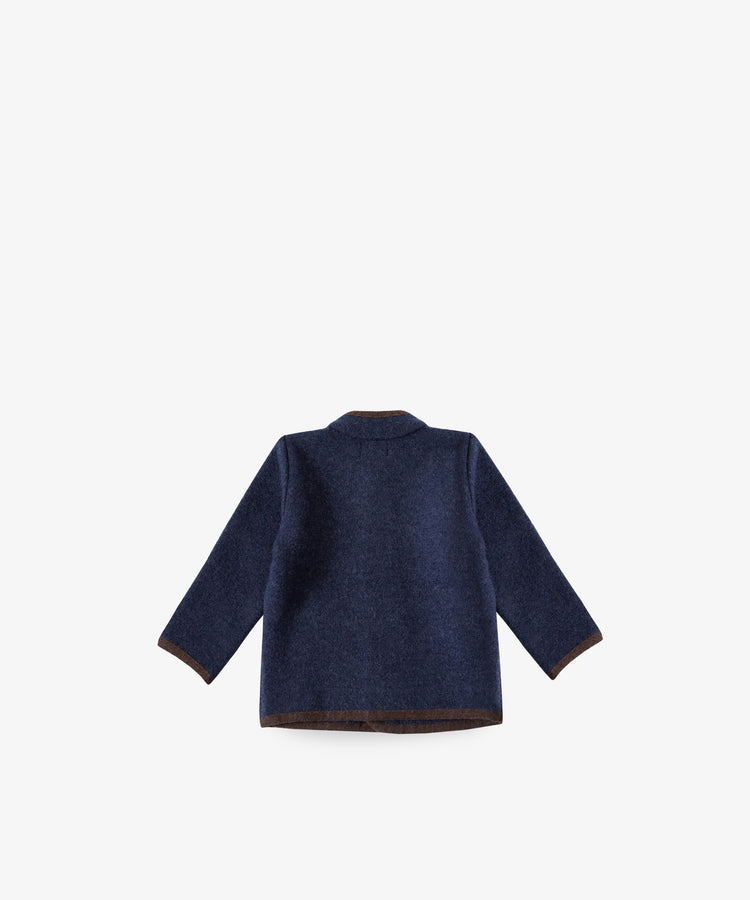 The Austrian Wool Jacket is a dark blue, long-sleeved coat with a Nehru collar and brown trim, inspired by Austrian children’s jackets. Pictured from the back against a plain white background.