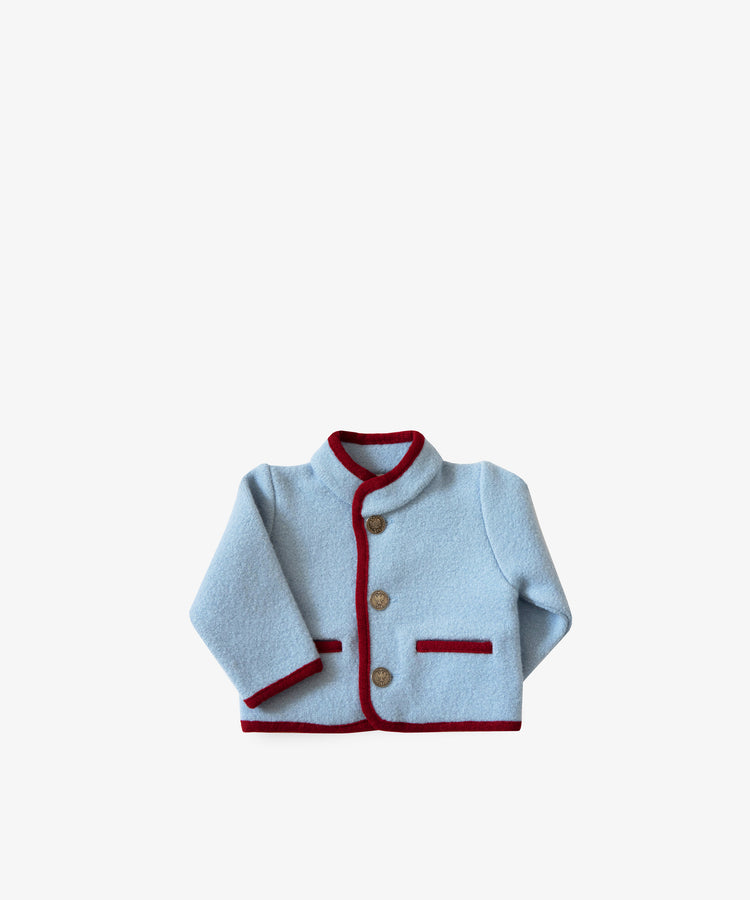 The Austrian Wool Jacket is a light blue children’s jacket made from soft merino wool, with brown buttons and a red trim on the collar, cuffs, hem, and pockets, shown against a plain white background.