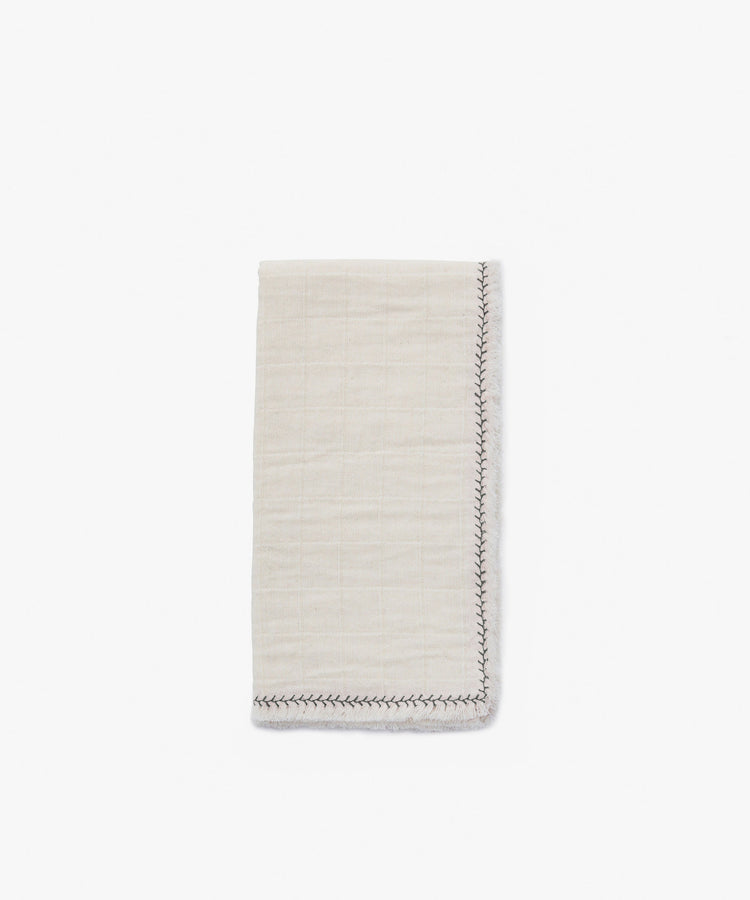 The Filial Napkin, Set of 6 features neatly folded, off-white cloth napkins with a subtle grid pattern and decorative branch stitch along the edge, displayed on a plain white tabletop.