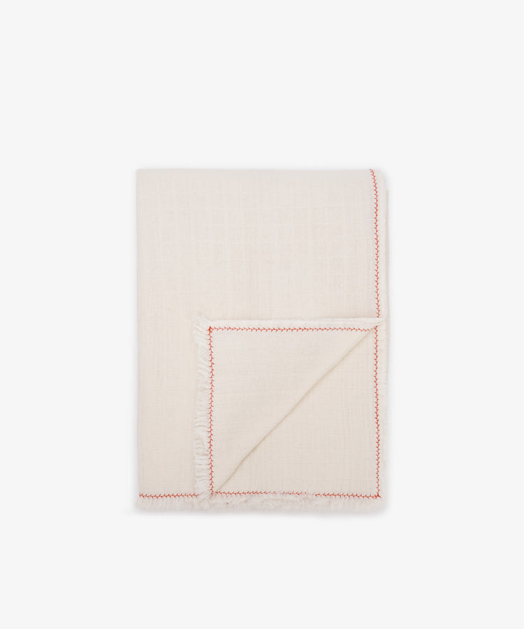 The Filial Tablecloth, crafted from natural weave fabric, features an off-white hue, frayed edges, and a red branch stitch along the border. It is shown folded on a plain white background.