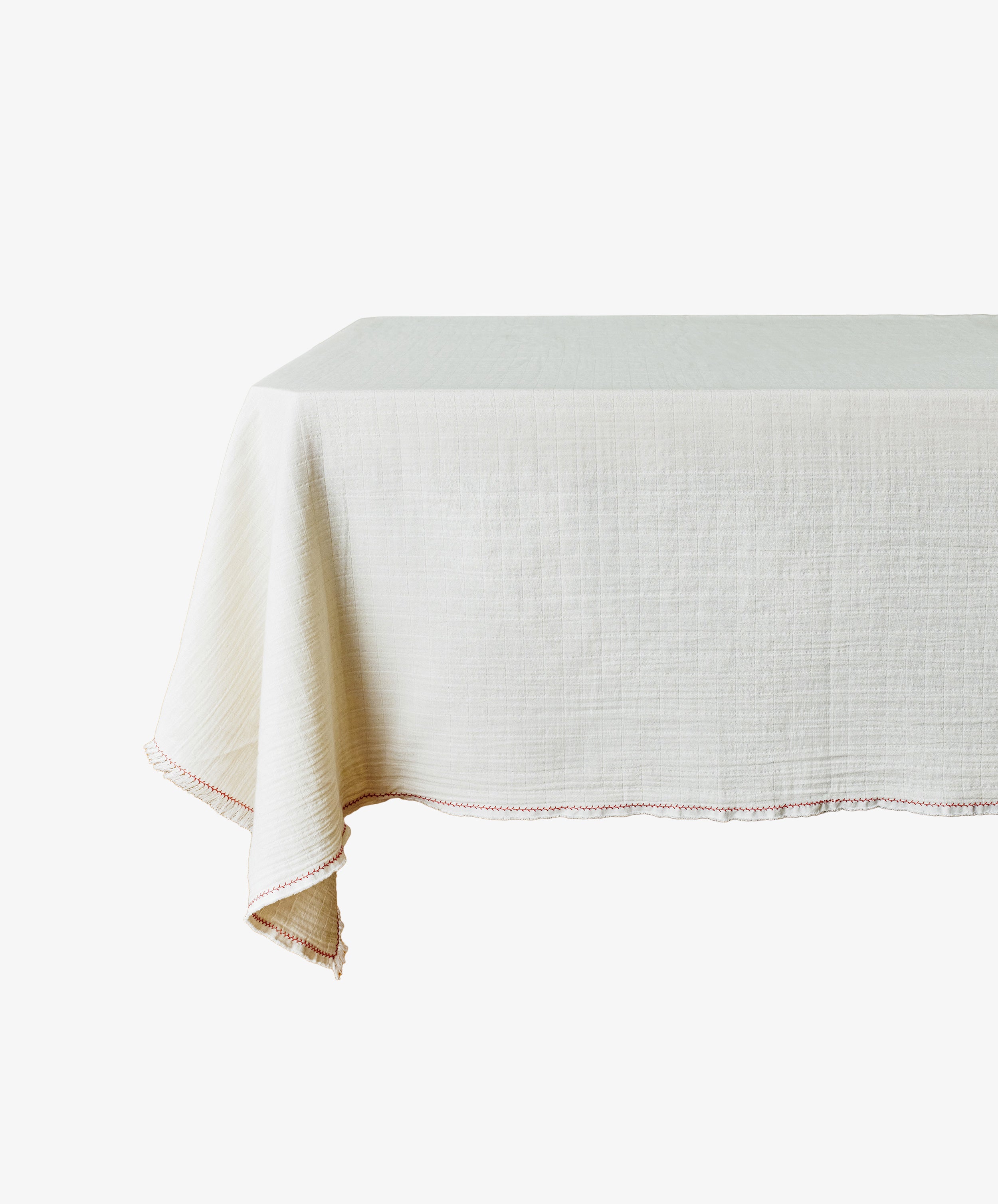 The Filial Tablecloth is a rectangular, off-white cloth with a natural weave texture and a simple red branch stitch border, minimally set on the table.