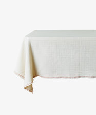 The Filial Tablecloth is a rectangular, off-white cloth with a natural weave texture and a simple red branch stitch border, minimally set on the table.