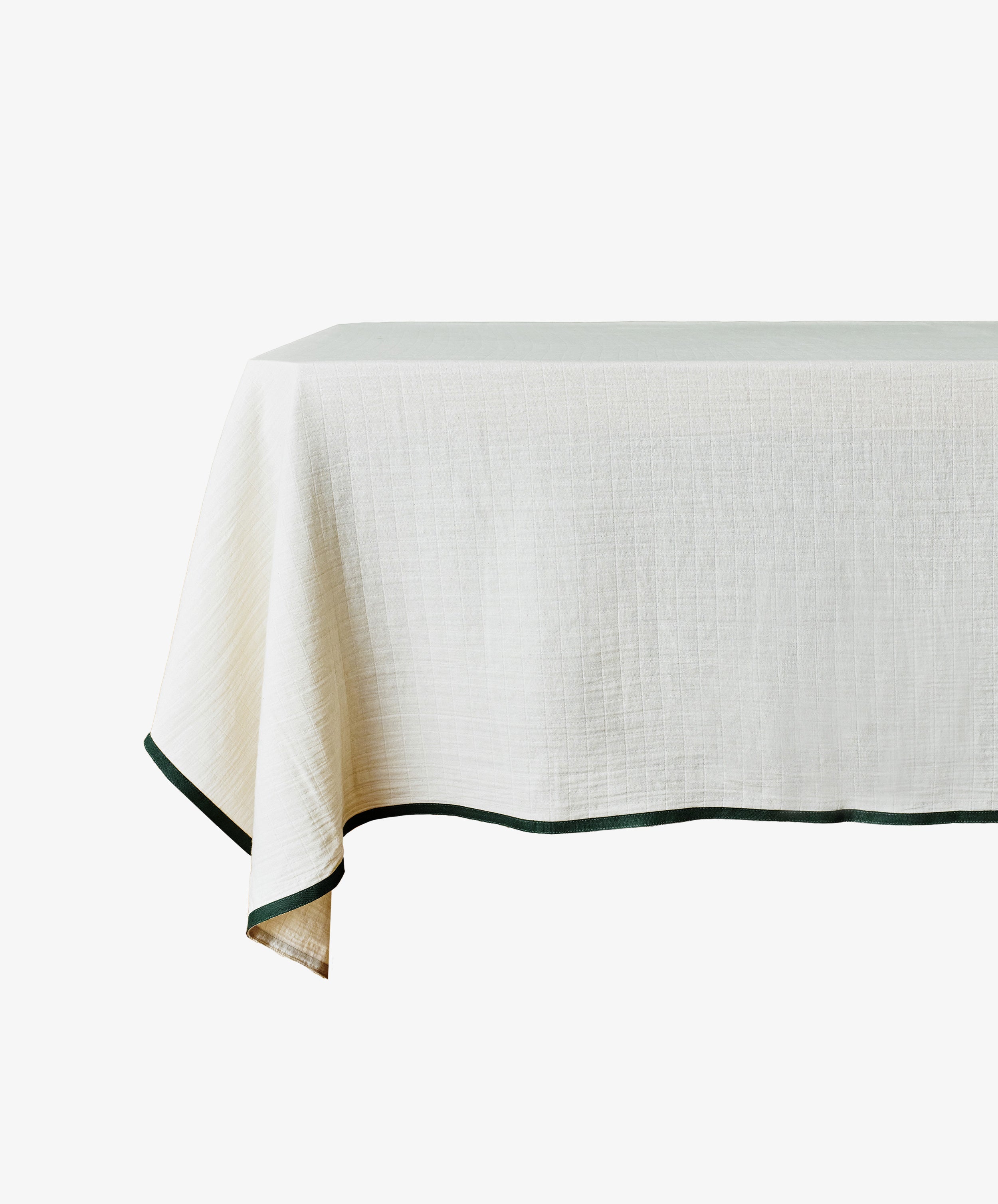 The Fita Tablecloth is a rectangular, natural cotton tablecloth in plain white with a dark green trim along the edge.