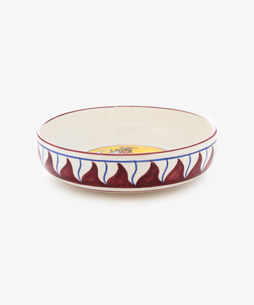 Palio Pasta Bowl in white glazed ceramic with burgundy and yellow accents and tower and elephant motif, side view.
