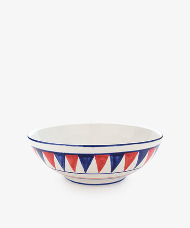 The Palio Serving Bowl, The Panther, is a shallow ceramic bowl with a white background and alternating red and blue triangles around the rim, inspired by the vibrant colors of the Siena Palio.
