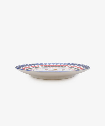 Palio Round Serving Platter. Large white glazed ceramic plate with blue and red accents and porcupine motif, side view.